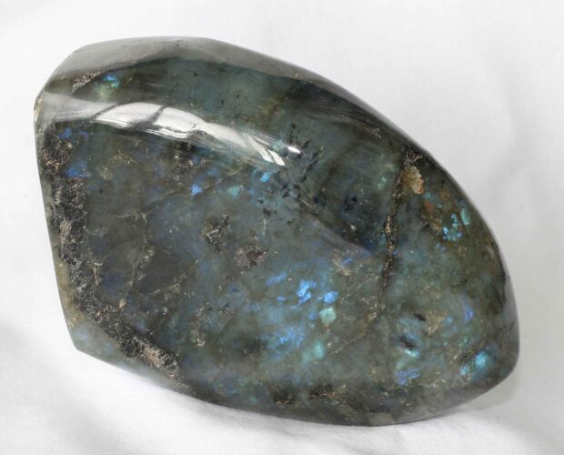 Polished labradorite stone showcasing blue and green iridescence on white surface