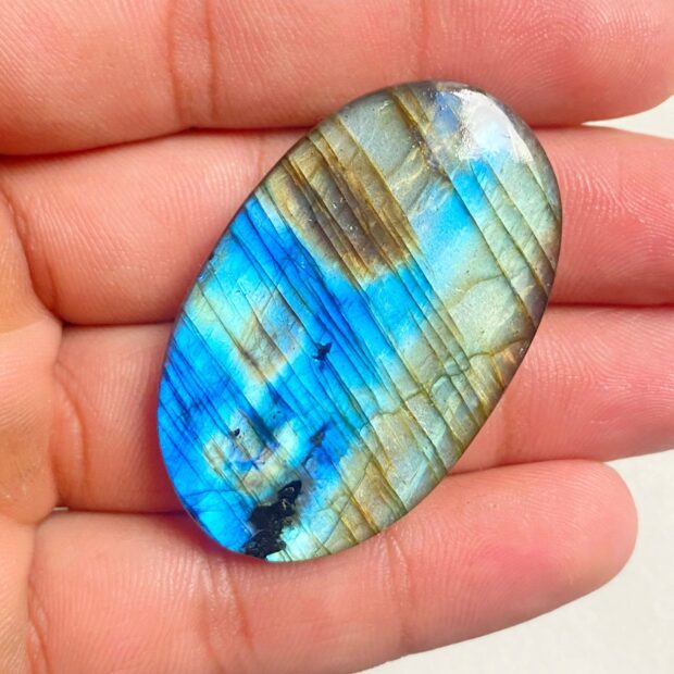 A polished labradorite stone with vibrant blue and green hues held in a hand