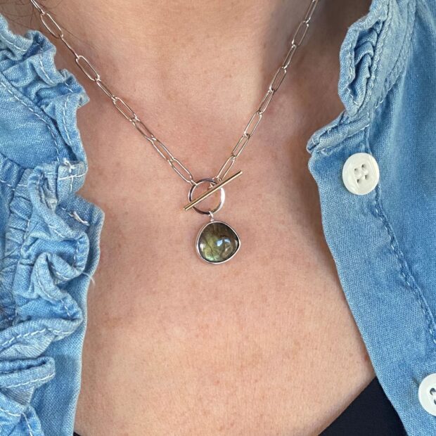 A close up of labradorite gemstone pendant on a silver chain necklace worn on a collarbone