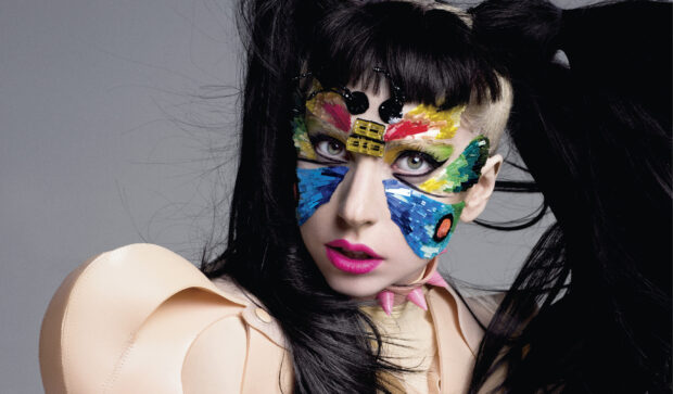 Lady Gaga with colorful face decorations and striking makeup looking at the camera