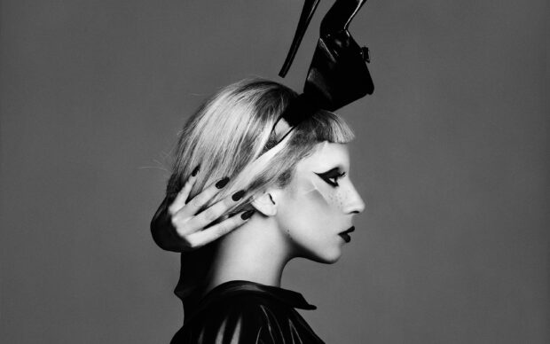 Lady Gaga in an artistic side profile with bold makeup and a high heel accessory on her head