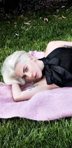 Lady Gaga lying on grass with platinum blonde hair and a black top