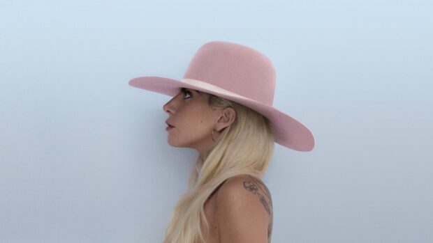 Lady Gaga with long blonde hair wearing a large pink hat and hoop earrings viewed from the side