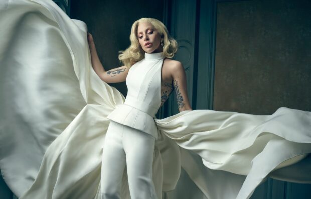 Lady Gaga wearing a flowing white outfit with visible tattoos on her arms indoors
