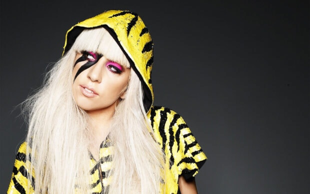 Lady Gaga wearing a yellow and black sequined hooded outfit with striking makeup and blonde hair