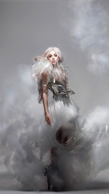 Lady Gaga wearing a futuristic outfit with long silver hair surrounded by mist
