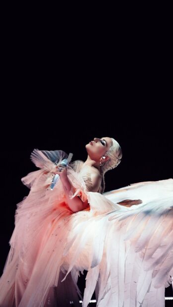 Lady Gaga wearing an angelic pink gown with large white feathers during a performance