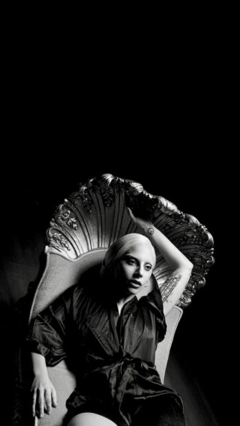 Lady Gaga lounging on a vintage chair wearing a dark outfit with visible tattoos on her arm