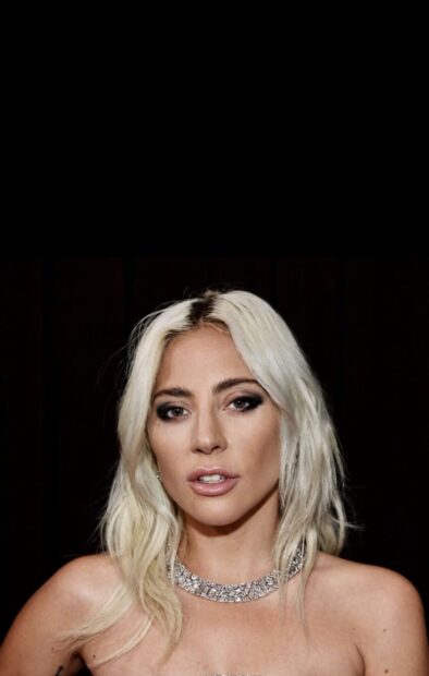 Lady Gaga with platinum blonde hair wearing a shiny necklace in a close up portrait