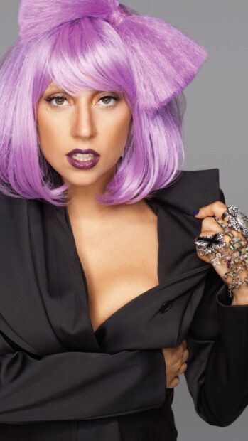 Lady Gaga with purple hair and bold makeup wearing a black outfit and statement rings