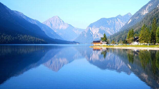 A serene lagoon landscape with clear blue water reflecting surrounding mountains and a small house nearby