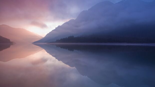 Calm lagoon surrounded by misty mountains during sunrise with soft light reflection