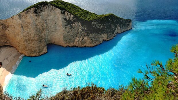 A stunning lagoon surrounded by cliffs and greenery with bright blue water and boats visible from above