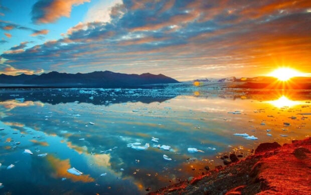 Beautiful lagoon scene with glowing sunset and scattered ice reflecting on the calm water