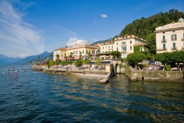 Historic buildings along Lake Como shore with mountains and clear blue sky