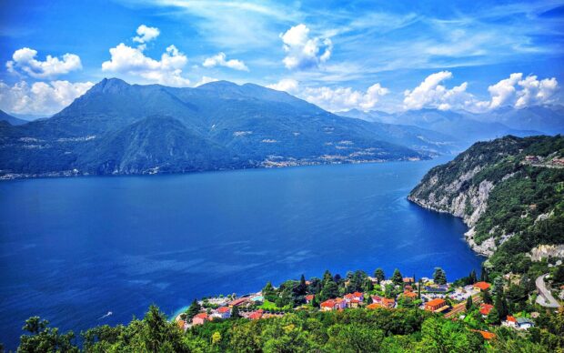 A panoramic view of Lake Como with lush greenery and mountainous landscape under a blue sky