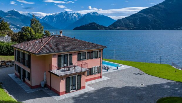 A pink house near water and mountains at Lake Como with clear blue sky