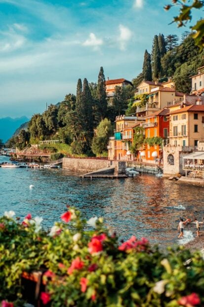 Colorful houses and lush greenery along Lake Como shore with flowers in foreground