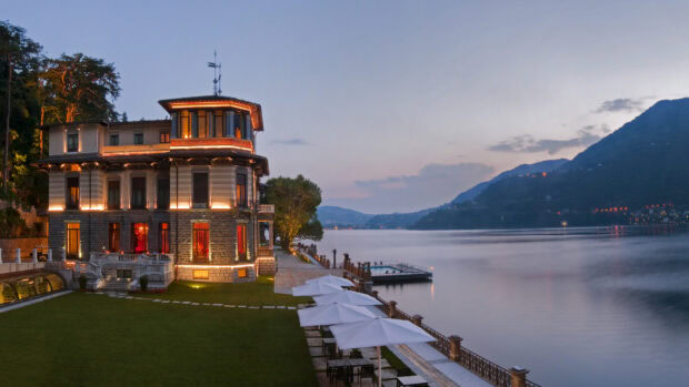 A historic villa near Lake Como with evening lights and calm water reflecting surrounding hills