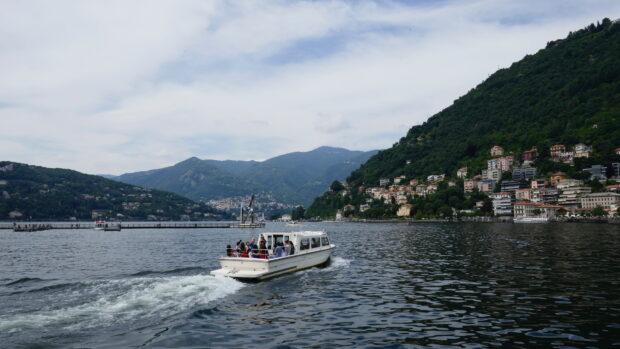 A boat carrying passengers on Lake Como with surrounding hills and buildings in the background
