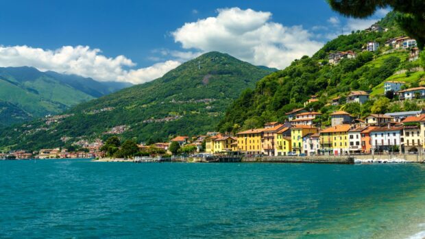 Colorful houses and green hills surround Lake Como in a scenic landscape