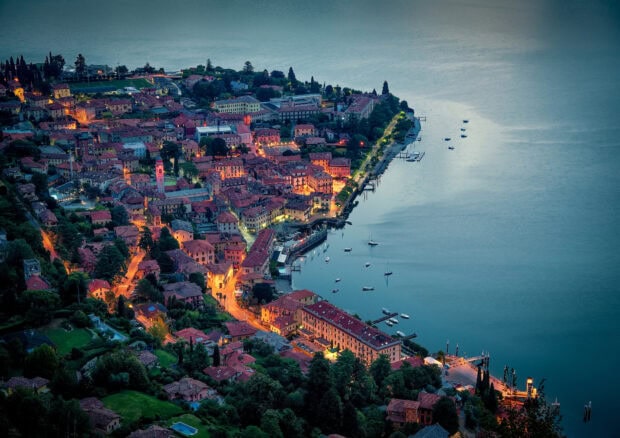 Evening view of Lake Como town with illuminated streets and calm watersurface