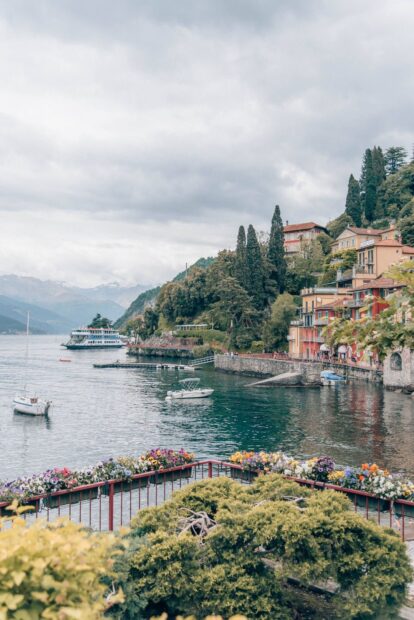 Colorful flowers and boats at Lake Como with scenic hillside village and cloudy sky