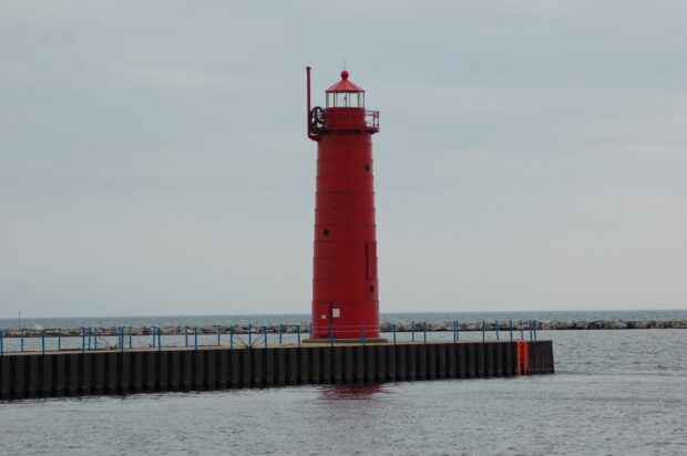 Red lighthouse standing on a pier along Lake Michigan under a cloudy sky