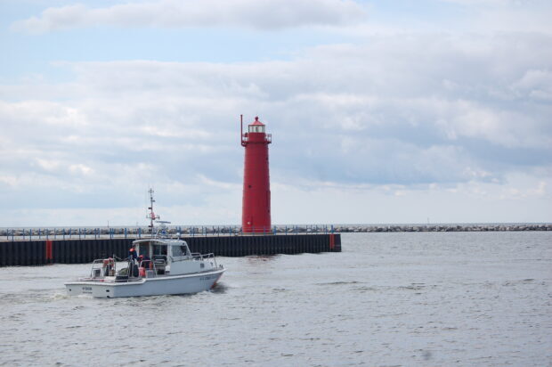 A red lighthouse stands near a pier on Lake Michigan with a US Coast Guard boat nearby