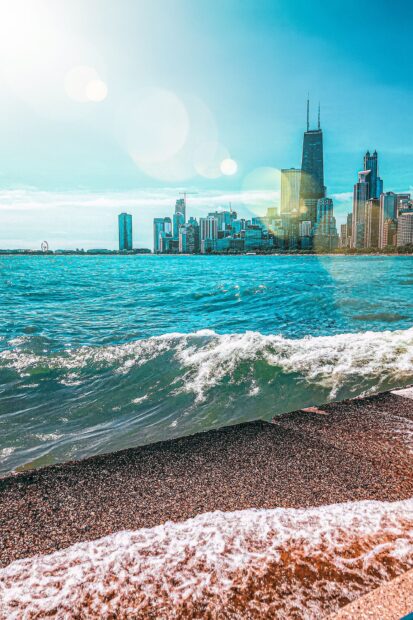 Waves crashing on Lake Michigan shore with city skyline in background under clear sky