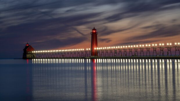 The calm lake Michigan with a long pier and lighthouse at sunset
