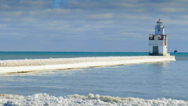 A snowy pier leading to a lighthouse on Lake Michigan under a cloudy sky