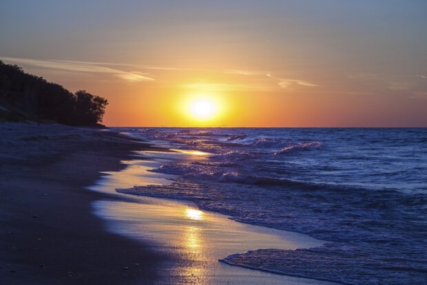 A peaceful sunset over Lake Michigan with waves gently hitting the sandy shore