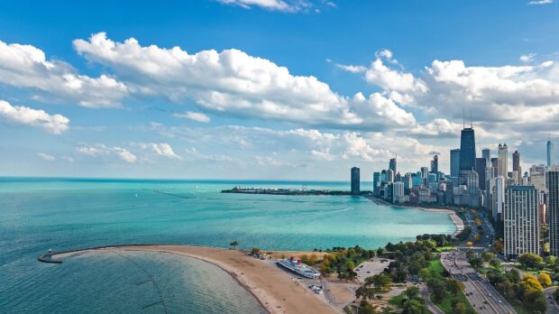 A clear view of Lake Michigan with a city skyline under a bright blue sky and scattered clouds