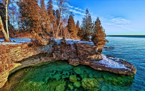Rocky shoreline with clear green water and trees near Lake Michigan shore in winter