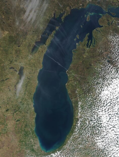 A satellite view of Lake Michigan surrounded by land and clouds in a natural landscape