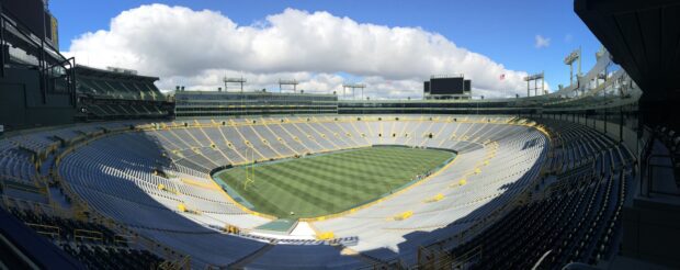 A panoramic view of Lambeau Field stadium showcasing the empty seats and green field under a partly cloudy sky