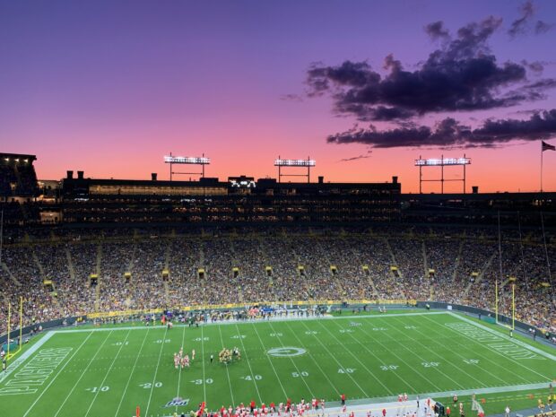 A panoramic view of Lambeau Field with a sunset sky and a packed crowd during a football game