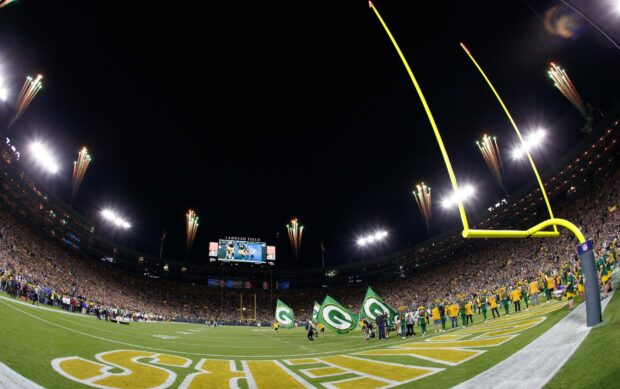 A wide view of Lambeau Field with fans and players celebrating on the field at night