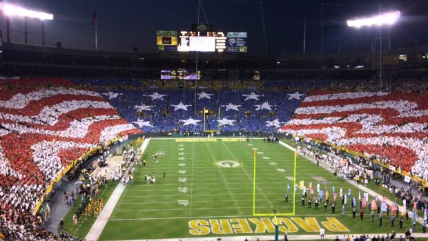 A panoramic view of Lambeau Field stadium filled with fans holding colored cards forming an American flag