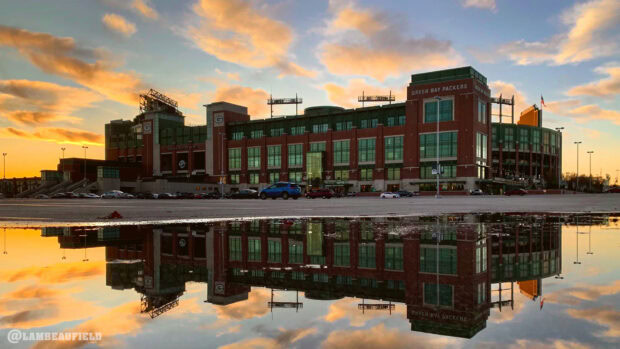 Lambeau Field stadium reflecting on a wet surface during sunset sky with Green Bay Packers signage