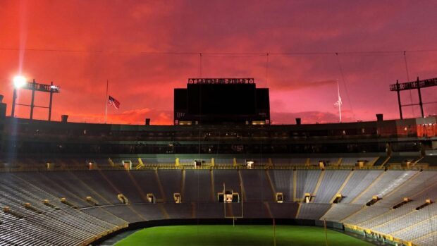 Lambeau Field stadium under a dramatic red sky at sunset with empty seats and American flags