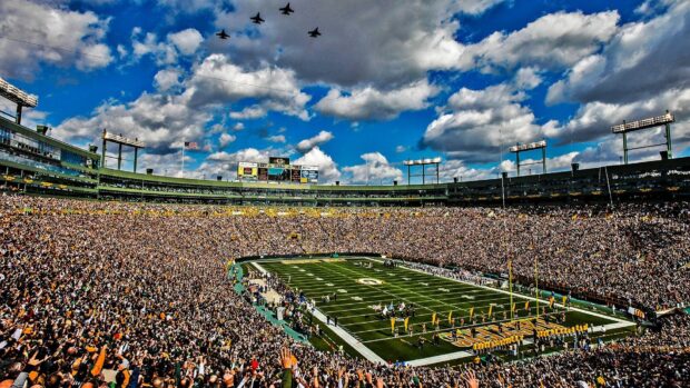 A large crowd fills Lambeau Field with jets flying overhead on a cloudy day