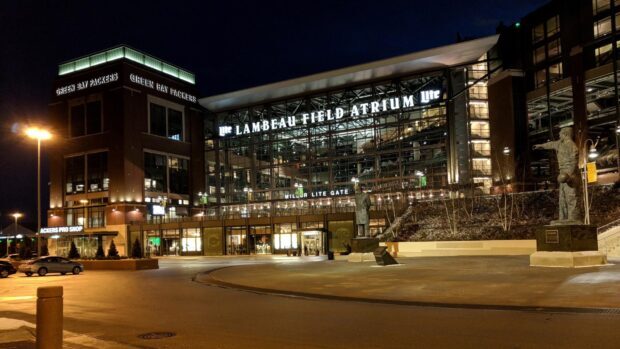 Lambeau Field atrium entrance at night showing Green Bay Packers statues and signage