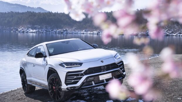 White Lamborghini Urus parked near a lake with trees in the background