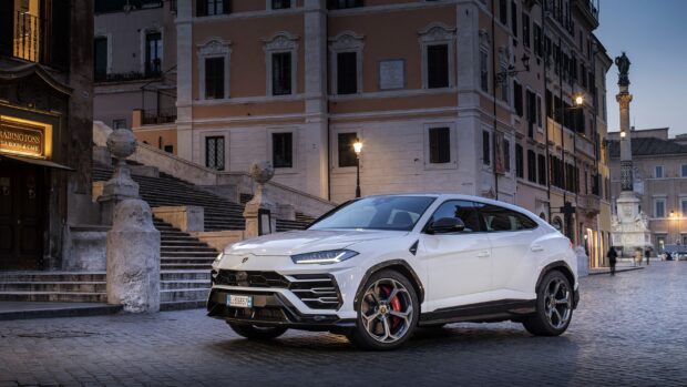 White Lamborghini Urus parked on a cobblestone street in front of historic buildings at dusk