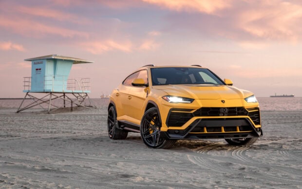 Yellow Lamborghini Urus standing on sandy beach near lifeguard tower at sunset with pink sky