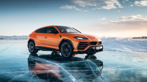 Orange Lamborghini Urus parked on icy surface with snowy mountains in the background