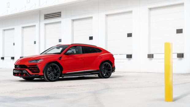 Red Lamborghini Urus parked in front of white garage doors in an empty lot