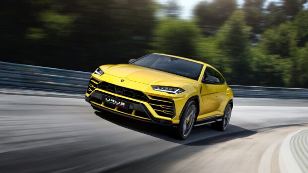 Yellow Lamborghini Urus driving fast on a curved racetrack surrounded by trees